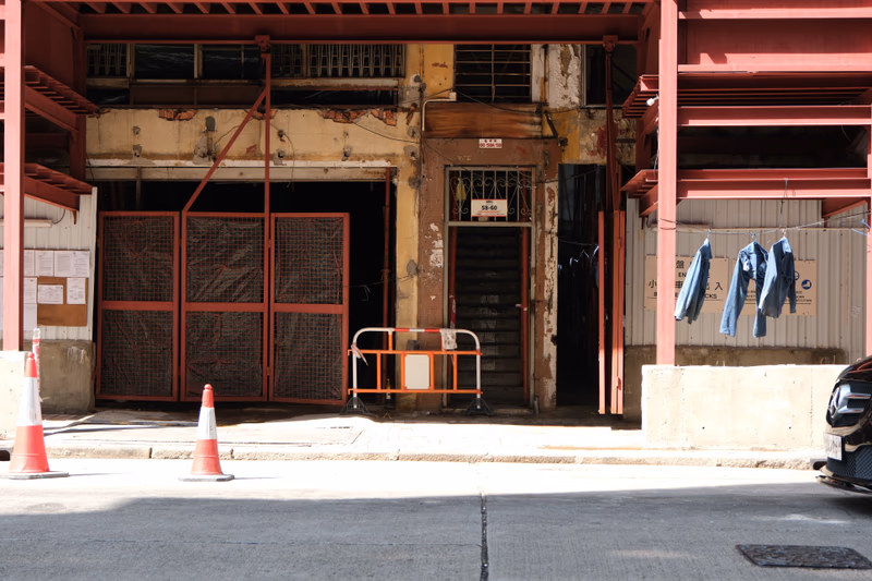 A photograph of a dilapidated building with a partially open door, cones placed on the street, and a sign in front.