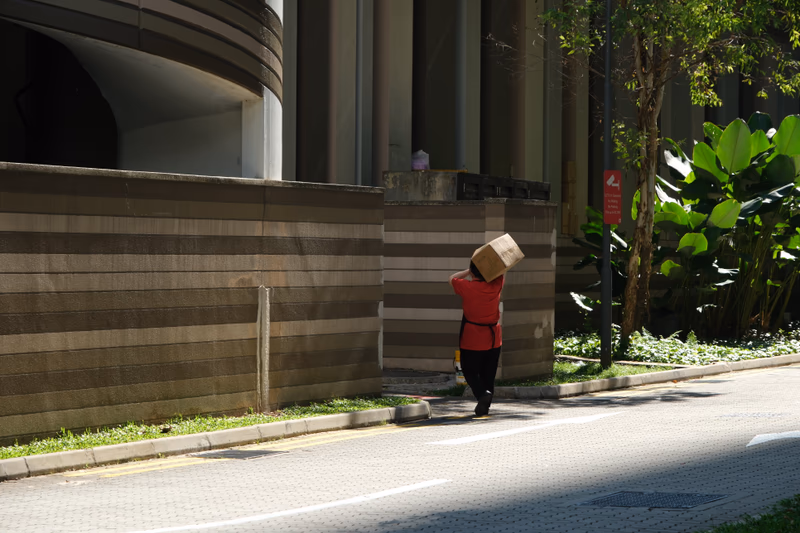 A person carrying a box on their head near a building.