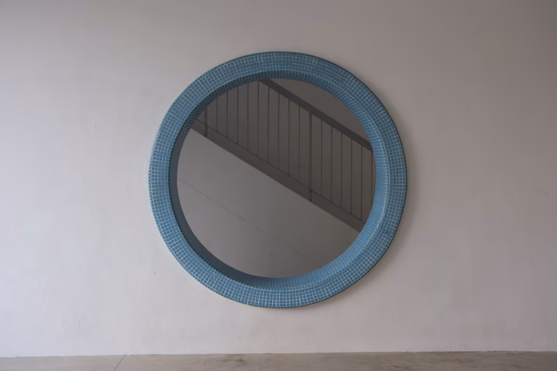 A circular mirror with a blue frame, reflecting a ceiling with vertical lines.